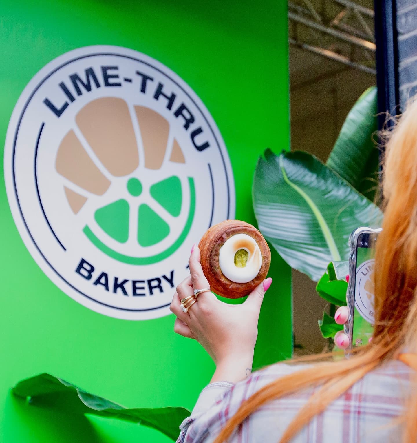 A customer holds up a lime cronut in front of the Lime-Thru Bakery branding