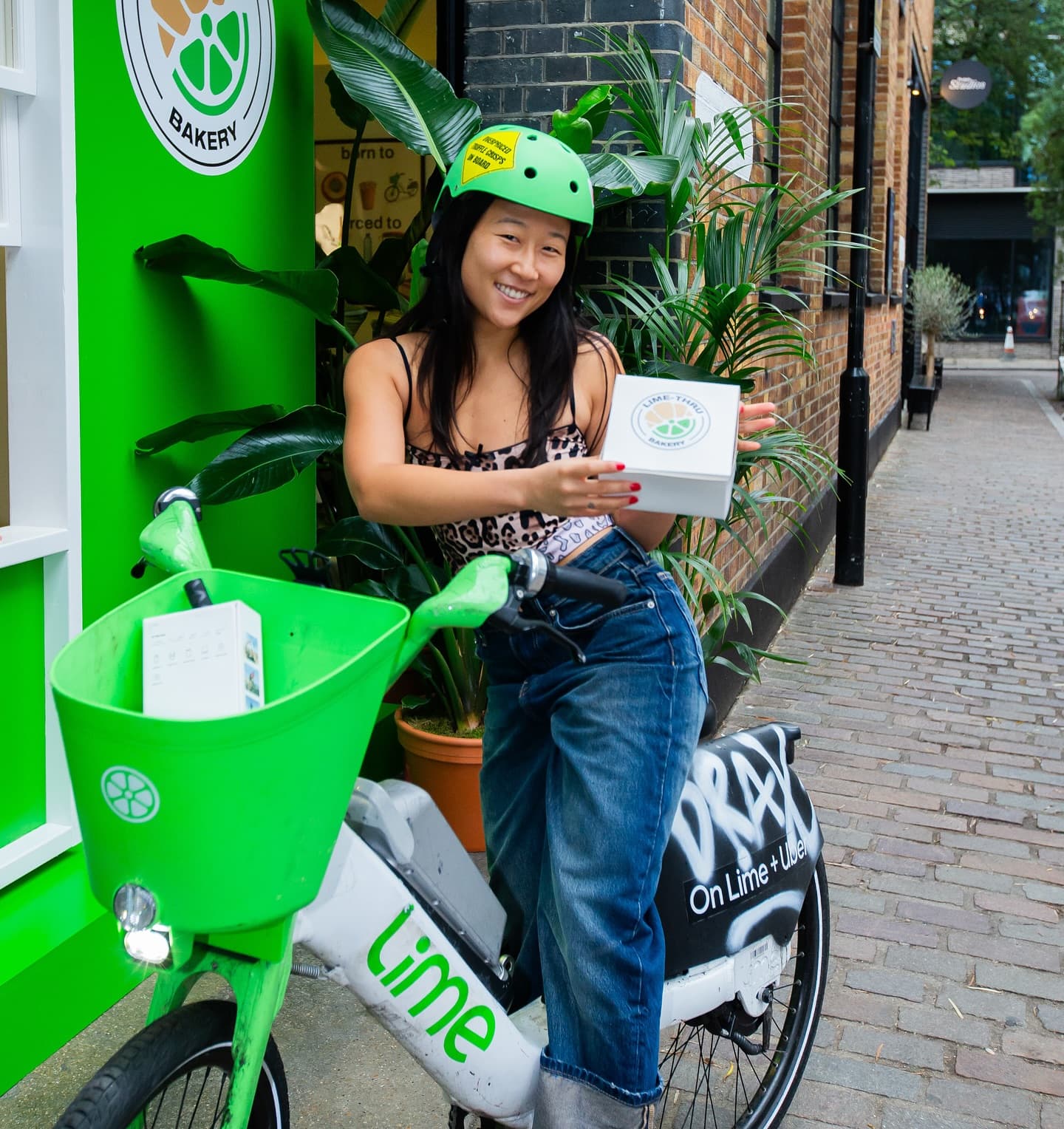 A Lime bike rider outside the pop-up holding a branded Lime-Thru Bakery cronut box