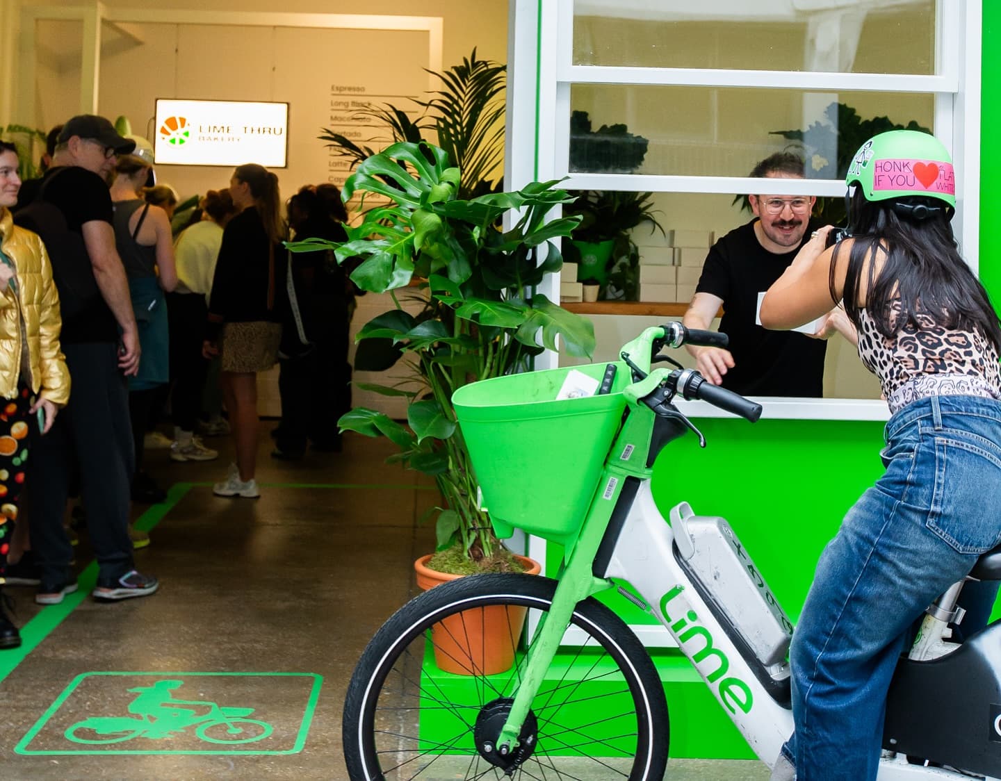 A Lime bike rider orders through the bike-through window while a barista serves coffee from inside