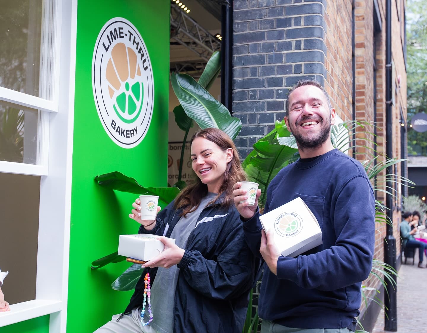 Two customers smiling with their coffees and cronut boxes outside the Lime-Thru Bakery pop-up in Shoreditch