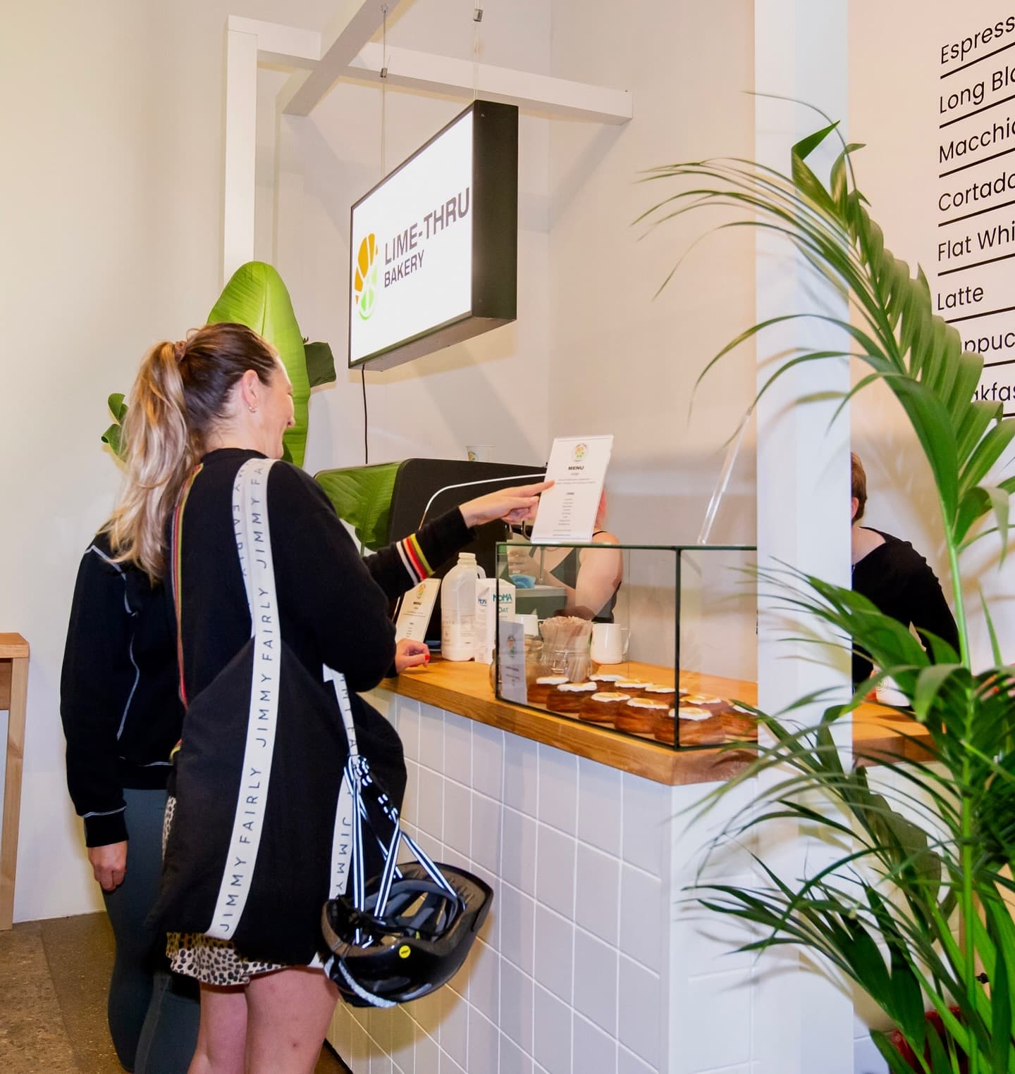 Inside the Lime-Thru Bakery pop-up: a customer orders at the tiled coffee bar with cronuts on display and a menu board on the wall