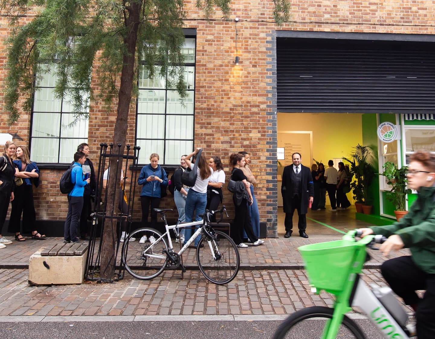 Queue of people waiting outside the Lime-Thru Bakery pop-up in Shoreditch, with a Lime bike rider passing in the foreground